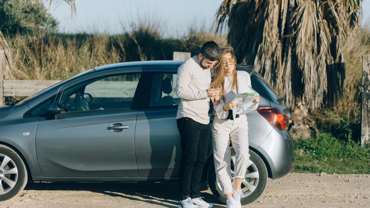 A couple standing by a car using a map to navigate during a sunny road trip.